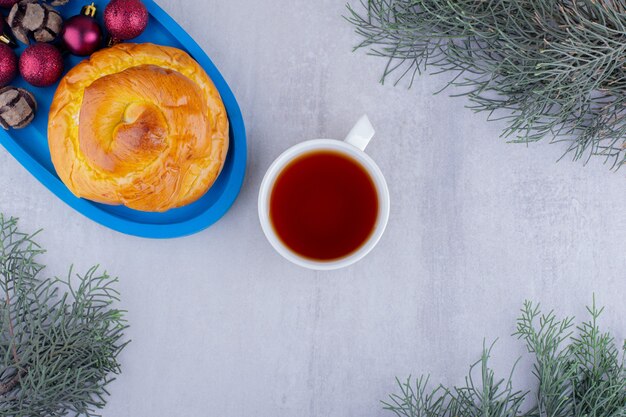 Blauwe schotel van zoet broodje en kerstversiering met een kopje thee op witte achtergrond.