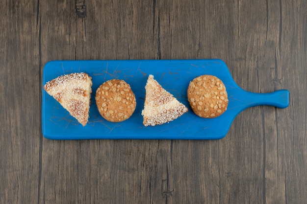 Blauwe snijplank van volkoren koekjes en zoete taart op houten tafel.