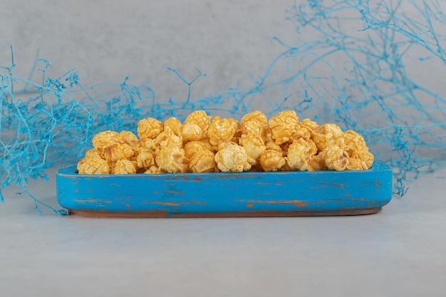 Gratis foto blauwe takken naast een kleine schotel van karamelpopcorn op marmeren tafel.
