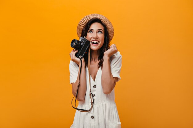 Blauwogige vrouw in de camera van de hoedenholding en verheugt zich op oranje achtergrond