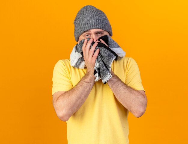 Bleke jonge blonde zieke Slavische man met winter hoed en houdt sjaal geïsoleerd op oranje muur met kopie ruimte