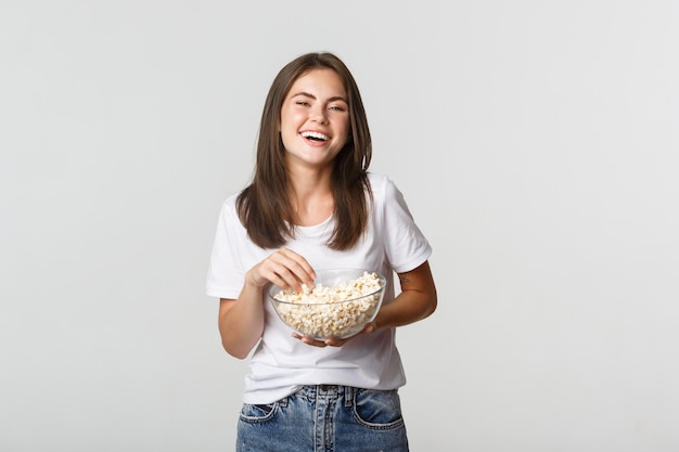 Blij aantrekkelijk donkerbruin meisje dat om komediefilm lacht, popcorn eet.