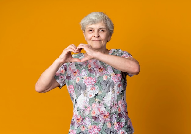 Blij bejaarde gebaren hart handteken geïsoleerd op oranje muur