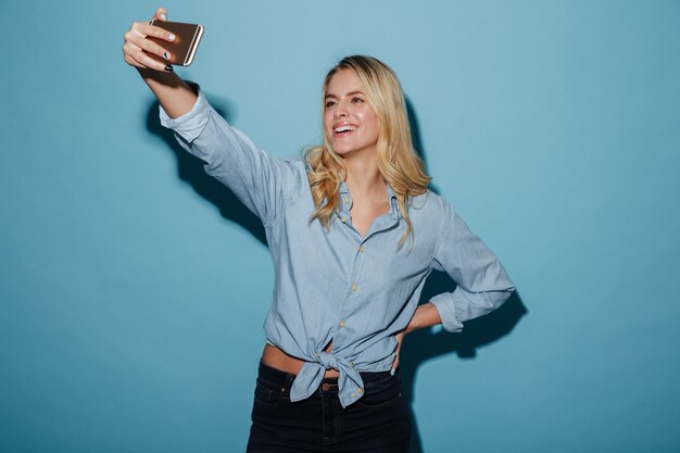 Blij blondevrouw die in overhemd selfie op smartphone maken