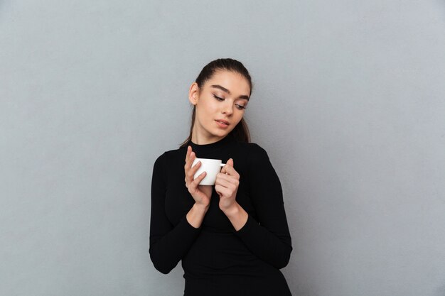 Blij brunette vrouw in zwarte kleding met kopje koffie