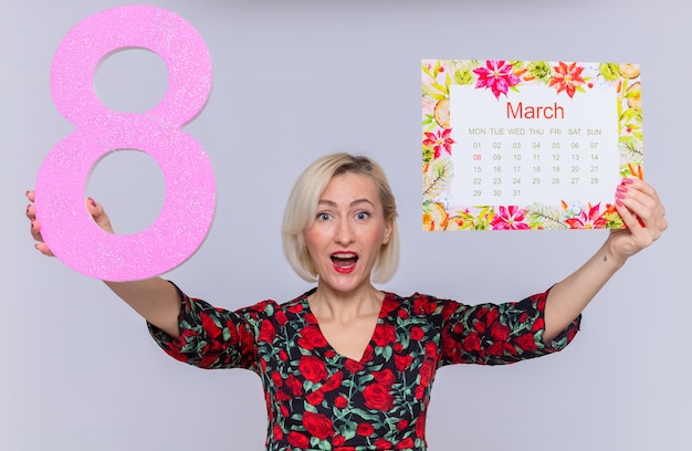 blij en verrast jonge vrouw met papieren kalender van de maand maart en nummer acht gemaakt van karton glimlachend vrolijk vieren internationale vrouwendag maart