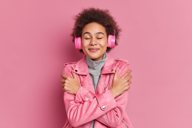 Gratis foto blij goed uitziend meisje met krullend afro haar ogen sluit omhelst zichzelf luistert naar muziek