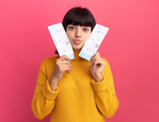 Blij jong brunette kaukasisch meisje houdt vliegtickets geïsoleerd op roze muur met kopieerruimte
