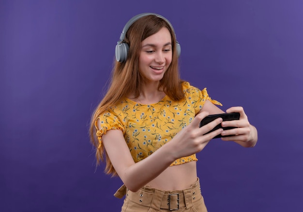 Blij jong meisje dat hoofdtelefoons draagt en mobiele telefoon op geïsoleerde purpere ruimte met exemplaarruimte houdt