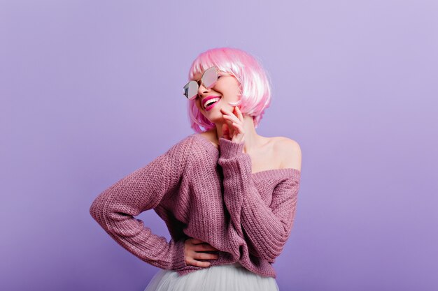 Blij jong meisje in periwig en zonnebril plezier Foto van prachtige vrouwelijke model met roze haar glimlachen tijdens het dansen op paarse muur.