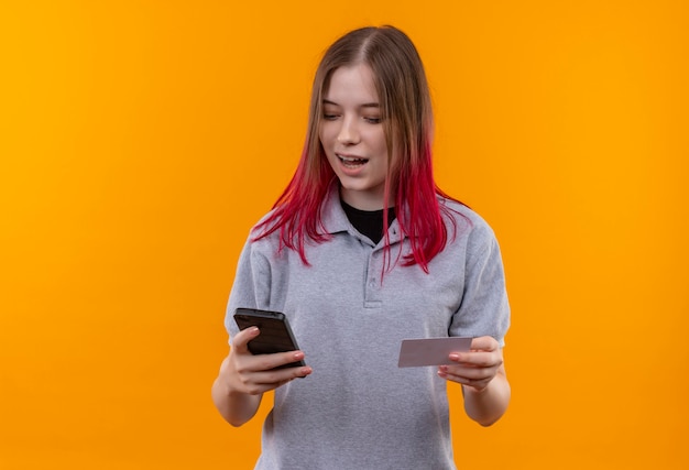 Blij jong mooi meisje dat het grijze nummer van het t-shirtnummer op telefoon op geïsoleerde gele achtergrond draagt