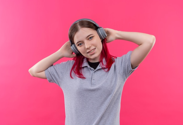 Blij jong mooi meisje met grijze t-shirt luisteren muziek op koptelefoon op geïsoleerde roze achtergrond