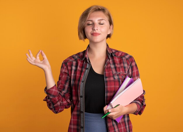 Blij jong slavisch studentenmeisje houdt een penboek vast en een notitieboekje doet alsof ze mediteert met gesloten ogen