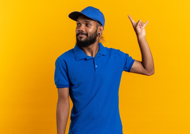 blij jonge bezorger gebaren hoorns en kijken naar kant geïsoleerd op oranje muur met kopie ruimte