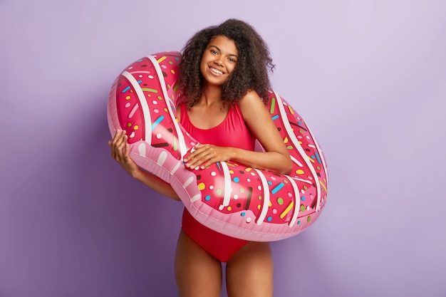 Blij jonge vrouw met krullend haar poseren met floaty zwembad