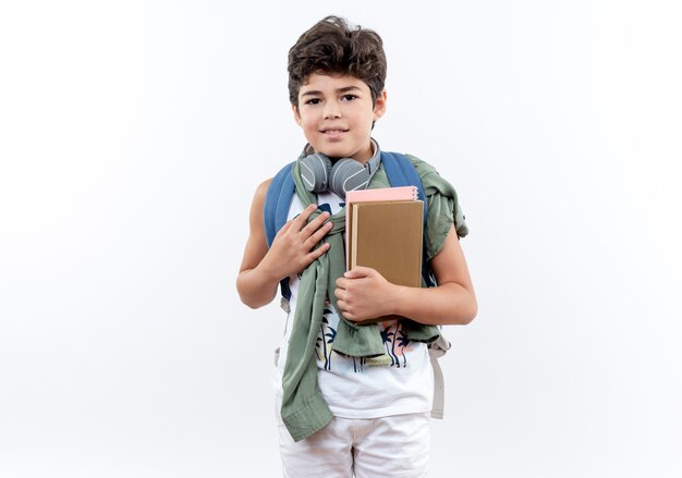 Blij kleine schooljongen met rugzak en koptelefoon met boek