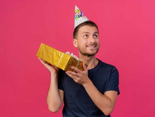 Blij knappe blanke man met verjaardag GLB houdt geschenkdoos kijken kant geïsoleerd op roze achtergrond met kopie ruimte