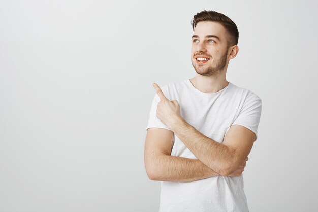 Blij knappe jongeman in wit t-shirt wijzende vinger linkerbovenhoek