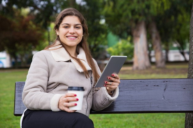 Blij Latijns universiteitsmeisje met tablet die meeneemkoffie drinken