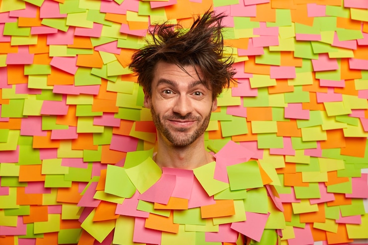 Gratis Foto blij mannelijk gezicht door gat in papieren muur met gekleurde stickers, heeft rommelig haar, stoppels, blij om iets leuks te horen, in goed humeur, dwazen rond. menselijke emoties en gevoelens concept