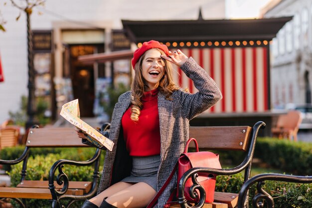 Blij meisje in een kort rokje zittend op een gezellig stadsplein en lachen