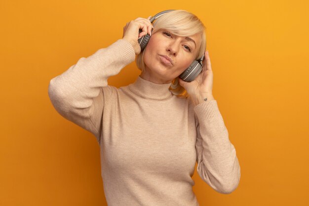 Blij mooie blonde Slavische vrouw op koptelefoon kijkt camera op oranje