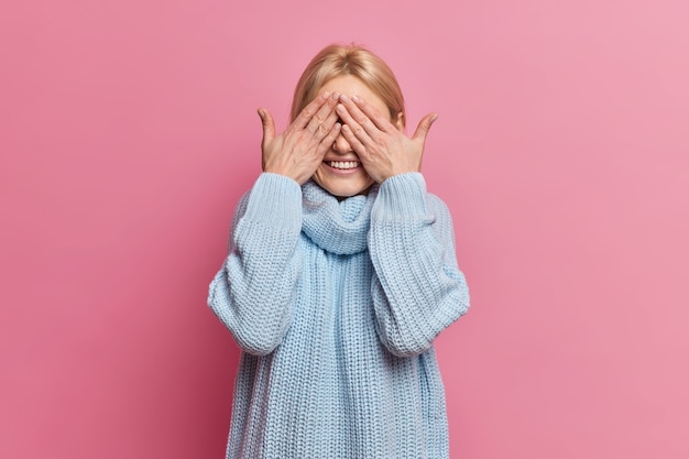 Blij speelse vrouw verbergt ogen met handen glimlacht vrolijk en wacht op een speciaal moment of verrassing