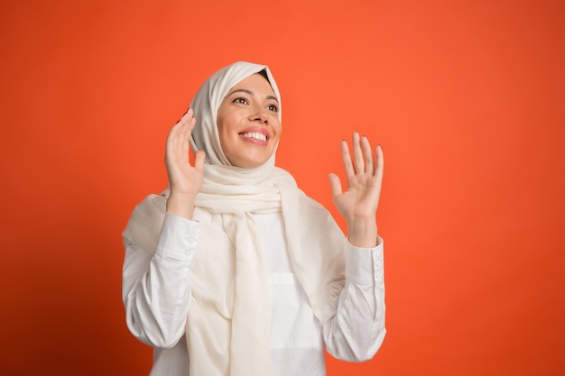 Blij verrast arabische vrouw in hijab. portret dat van glimlachend meisje, bij rode studioachtergrond stelt. jonge emotionele vrouw. menselijke emoties, gezichtsuitdrukking concept.