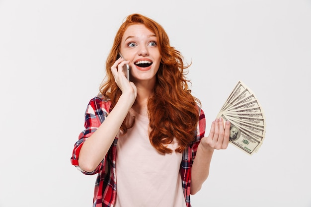 Blij verraste gembervrouw in overhemd die door smartphone spreken terwijl geld houden en weg het kijken