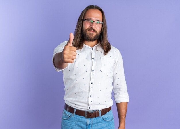 Blij volwassen knappe man met een bril kijkend naar de camera met duim omhoog geïsoleerd op paarse muur met kopieerruimte