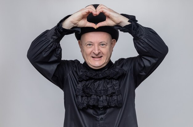 Blij volwassen Slavische man met hoge hoed en in zwarte gotische shirt gebaren hart teken