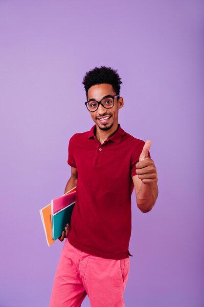 Blije Afrikaanse student met stijlvol kapsel die geniet van fotoshoot na examens Studioportret van knappe jongeman met boeken