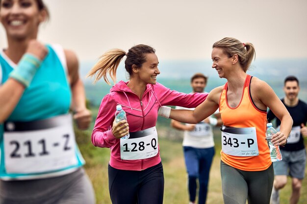 Blije atletische vrouwen die elkaar steunen tijdens het lopen van een marathon in de natuur