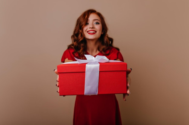 Blije gembervrouw die poseert met een kerstcadeau Winsome roodharige meid die een nieuwjaarscadeau vasthoudt en lacht