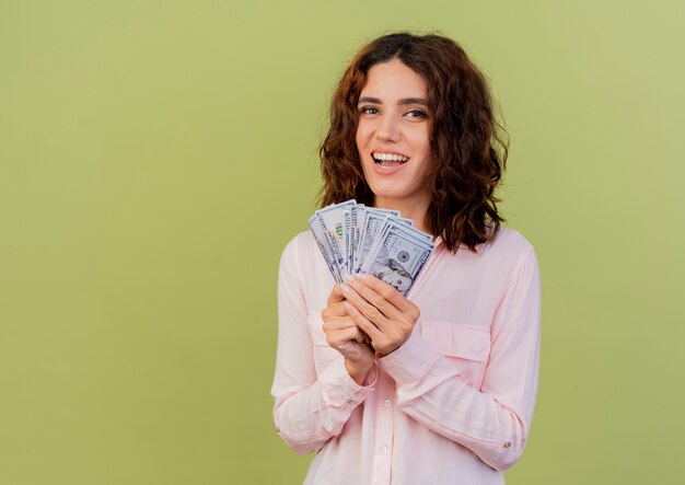 Blije jonge blanke vrouw houdt geld kijken camera geïsoleerd op groene achtergrond met kopie ruimte