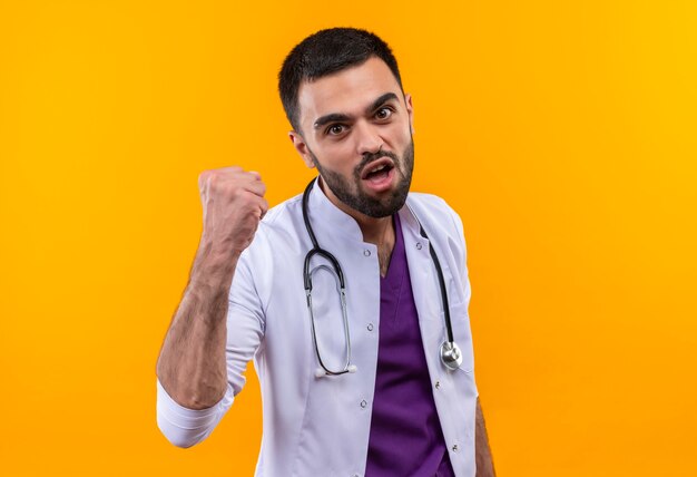 Blije jonge mannelijke arts die stethoscoop medische toga draagt die ja gebaar op geïsoleerde gele muur toont