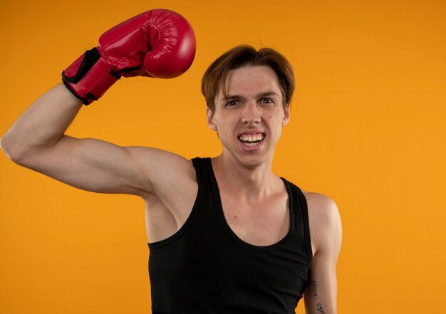 Blije jonge sportieve kerel die bokshandschoenen draagt die hand opheffen die op oranje muur wordt geïsoleerd