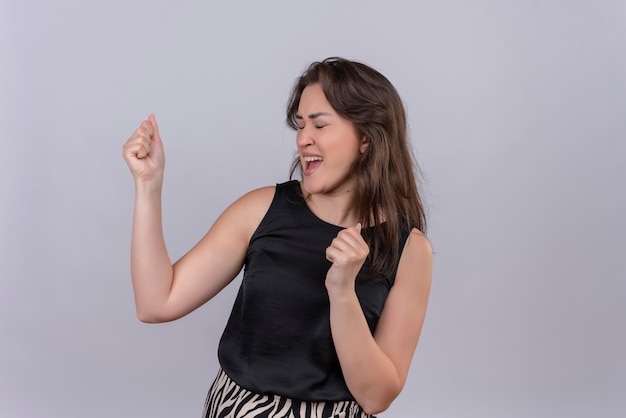 Blije jonge vrouw die zwart hemd draagt dat op witte muur danst