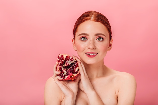 Blije jonge vrouw met granaat studio shot van naakt meisje met rijpe granaatappel geïsoleerd op roze achtergrond