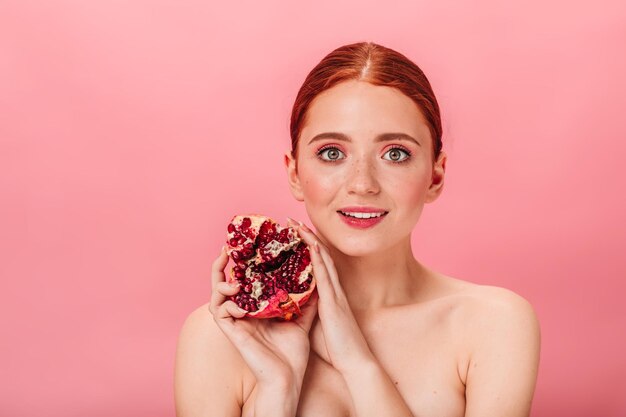 Blije jonge vrouw met granaat Studio shot van naakt meisje met rijpe granaatappel geïsoleerd op roze achtergrond