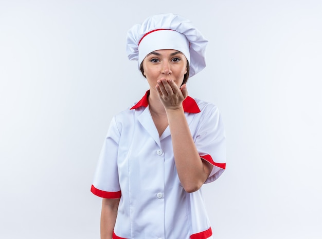 Blije jonge vrouwelijke kok die chef-kok uniform draagt ??die kusgebaar toont dat op witte achtergrond wordt geïsoleerd