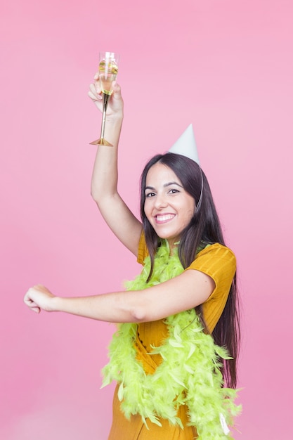 Blije Kaukasische vrouw die met opgeheven glas champagne tegen roze achtergrond danst