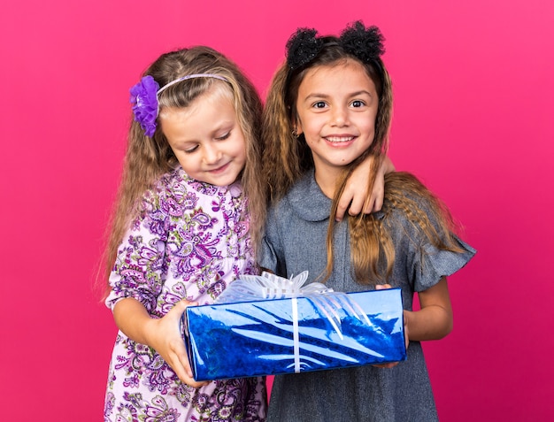blije kleine mooie meisjes die een geschenkdoos bij elkaar houden geïsoleerd op een roze muur met kopieerruimte