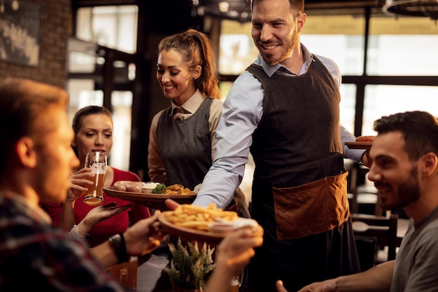 Blije obers die eten aan tafel brengen en een groep vrienden bedienen in een restaurant