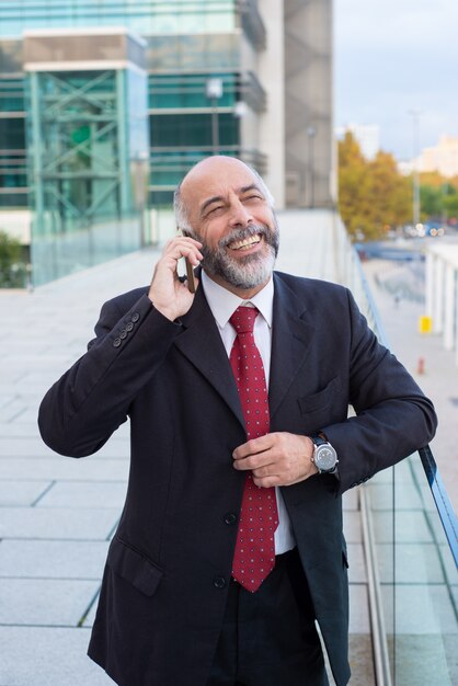 Blije succesvolle rijpe zakenman die op cellphone spreekt