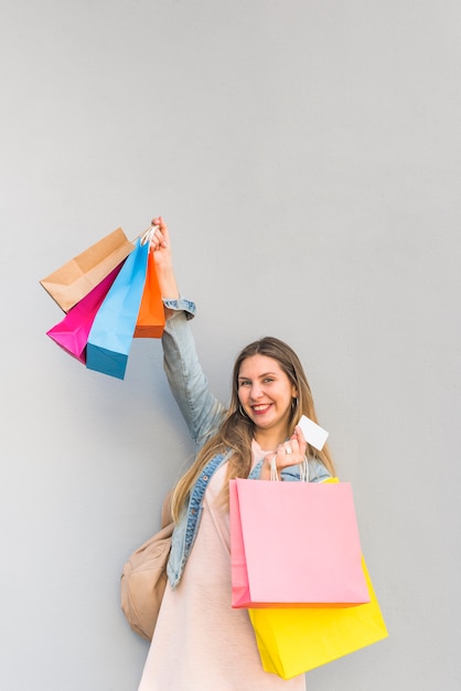 Blije vrouw die zich met het winkelen zakken en creditcard bij lichte muur bevindt