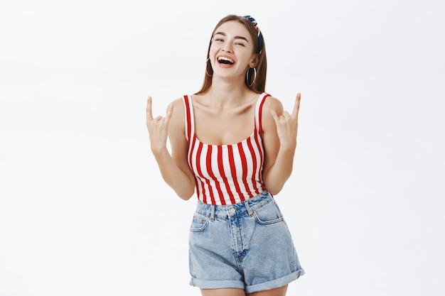 Blije zorgeloze stijlvolle pinup vrouw in gestreepte top en denim shorts met rock n roll gebaar lachen