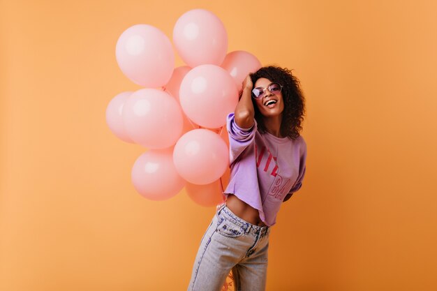 Blithesome Afrikaanse dame dansen op evenement. blij verjaardag meisje poseren op oranje met een heleboel ballonnen.