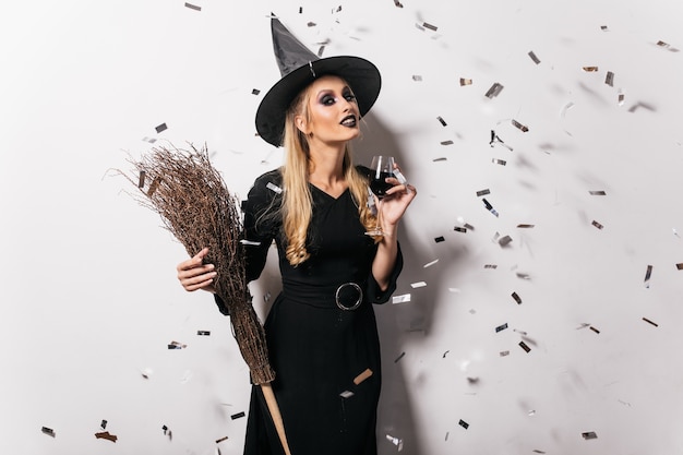 Blithesome jonge heks die wijn drinkt. Zorgeloze vrouw in halloween-kleding die zich voordeed op feestje.