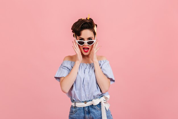 Blithesome pinup meisje poseren in zonnebril. Studio shot van jonge vrouw in blauw gestreepte blouse.